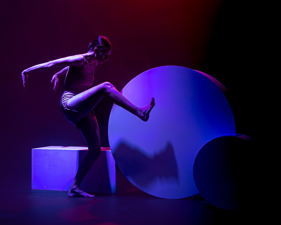 “Elisa, bailarina contemporánea posando entre formas geométricas iluminadas en tonos rojos, violetas y azules durante una sesión fotográfica artística.”
