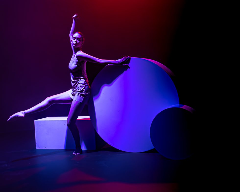 “Elisa, bailarina contemporánea posando entre formas geométricas iluminadas en tonos rojos, violetas y azules durante una sesión fotográfica artística.”