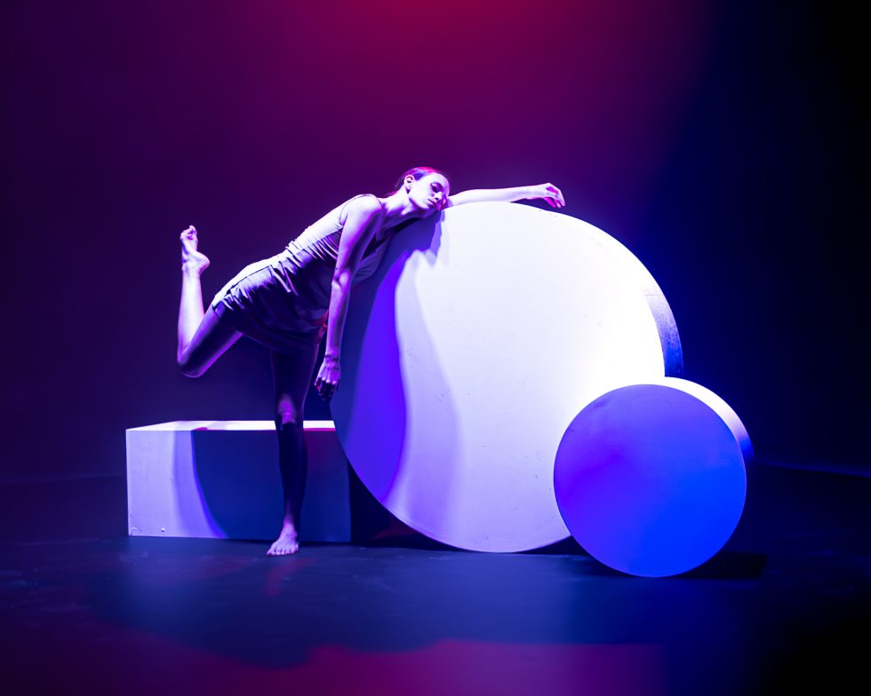 “Elisa, bailarina contemporánea posando entre formas geométricas iluminadas en tonos rojos, violetas y azules durante una sesión fotográfica artística.”