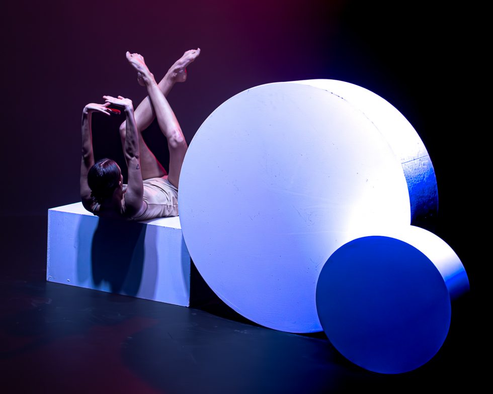 “Elisa, bailarina contemporánea posando entre formas geométricas iluminadas en tonos rojos, violetas y azules durante una sesión fotográfica artística.”