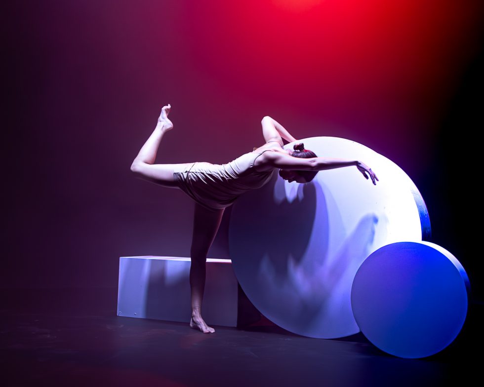 “Elisa, bailarina contemporánea posando entre formas geométricas iluminadas en tonos rojos, violetas y azules durante una sesión fotográfica artística.”