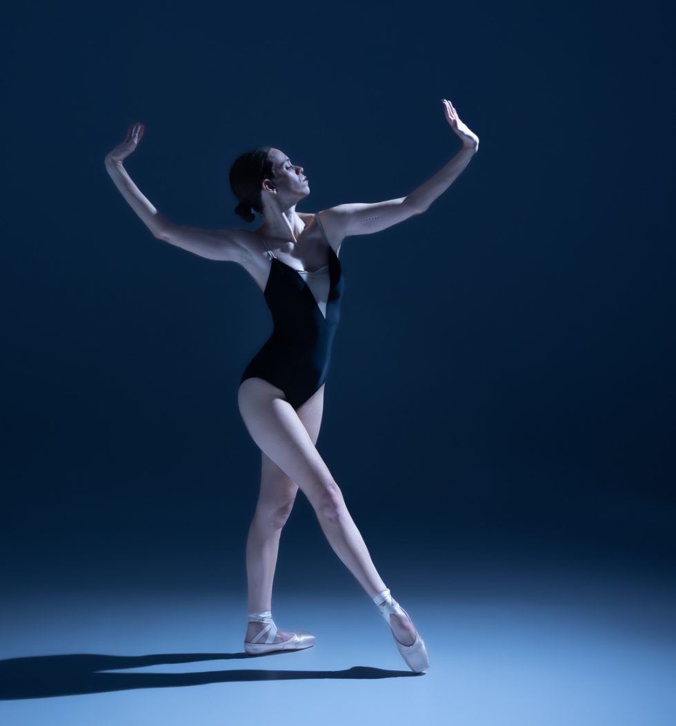 “Bailarina Elisa ejecutando poses de danza clásica y contemporánea sobre punta en estudio, iluminada en tonos azules.”