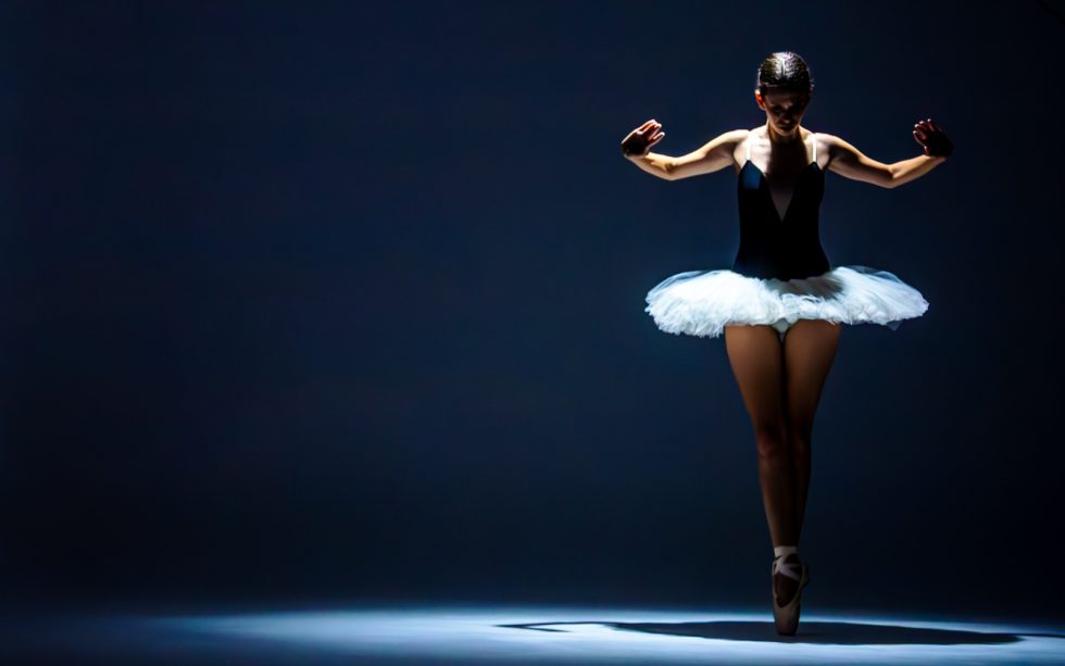 “Bailarina de ballet interpretando poses expresivas con tutú blanco y luz dramática sobre fondo oscuro.”