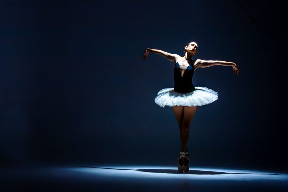 “Bailarina de ballet interpretando poses expresivas con tutú blanco y luz dramática sobre fondo oscuro.”