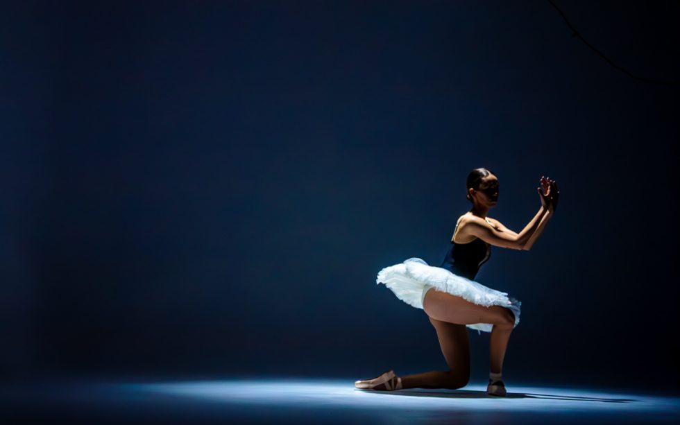 “Bailarina de ballet interpretando poses expresivas con tutú blanco y luz dramática sobre fondo oscuro.”