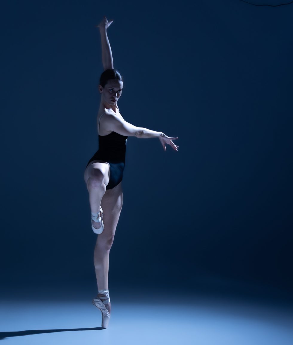 “Bailarina Elisa ejecutando poses de danza clásica y contemporánea sobre punta en estudio, iluminada en tonos azules.”