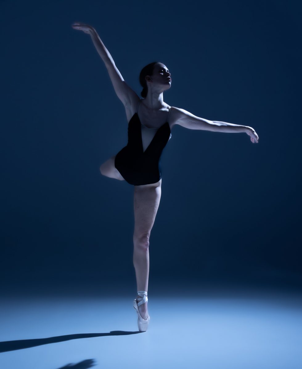 “Bailarina Elisa ejecutando poses de danza clásica y contemporánea sobre punta en estudio, iluminada en tonos azules.”