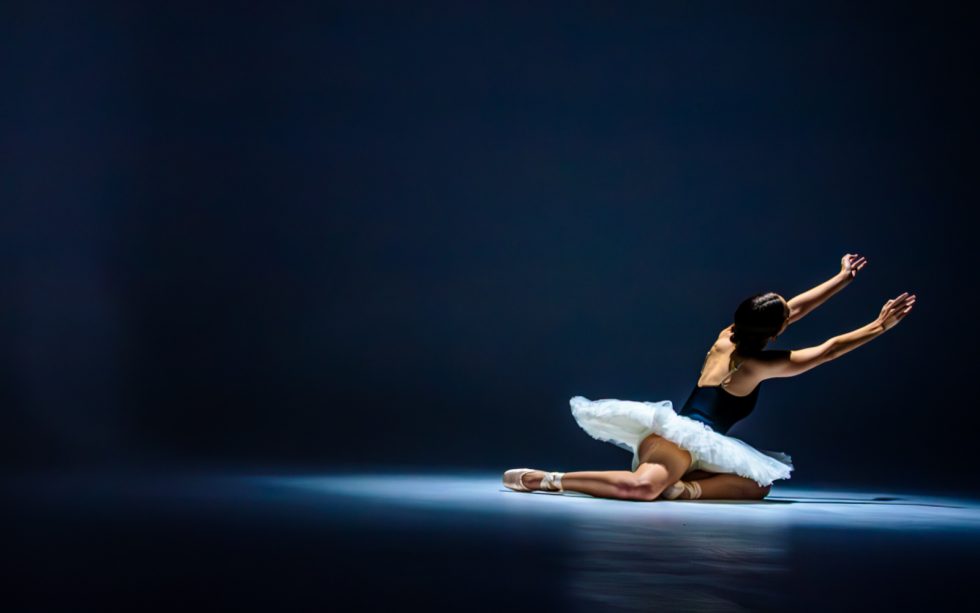 “Bailarina de ballet interpretando poses expresivas con tutú blanco y luz dramática sobre fondo oscuro.”