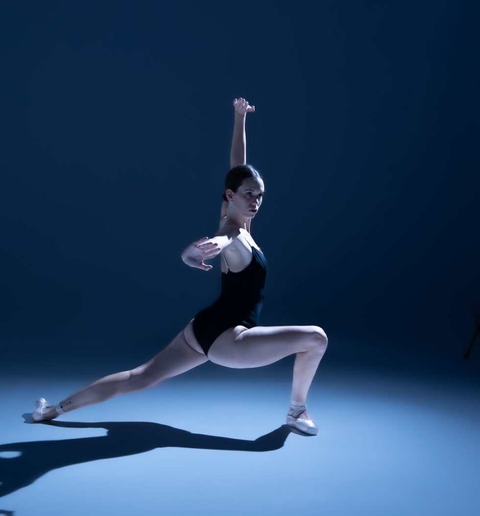 “Bailarina Elisa ejecutando poses de danza clásica y contemporánea sobre punta en estudio, iluminada en tonos azules.”
