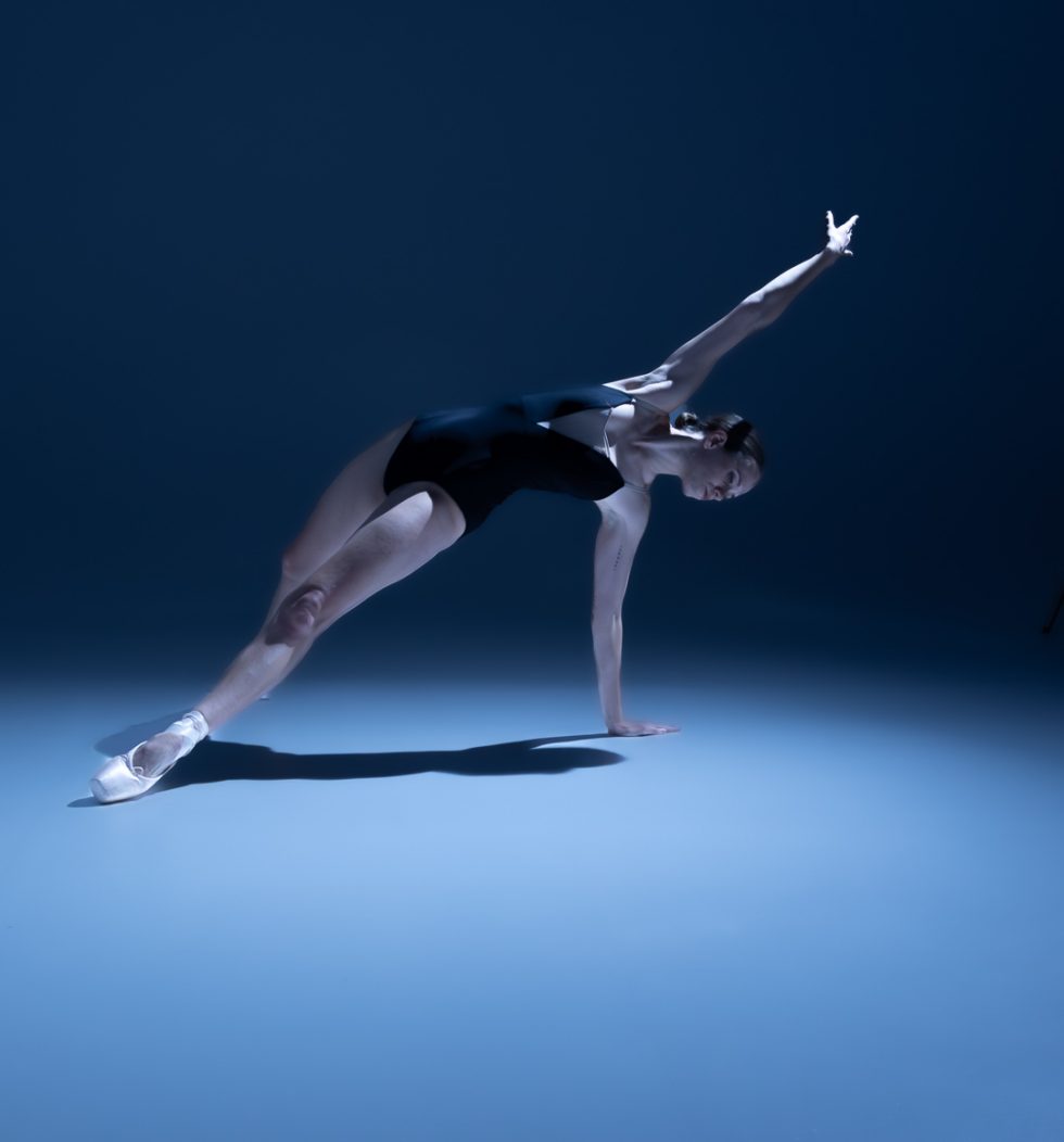 “Bailarina Elisa ejecutando poses de danza clásica y contemporánea sobre punta en estudio, iluminada en tonos azules.”