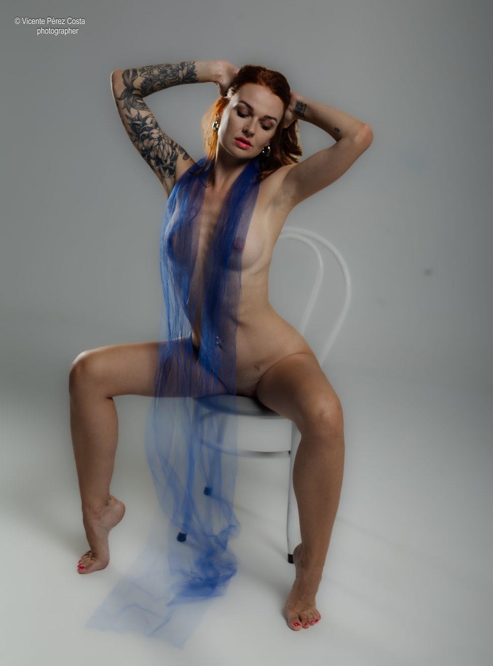 “Modelo posando en estudio con tela azul en una sesión de desnudo artístico, iluminada en clave suave y con estética minimalista.”