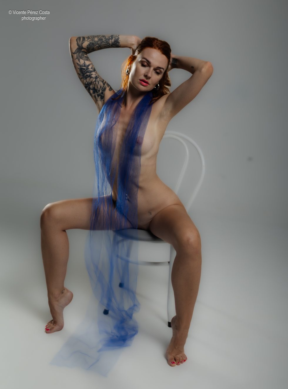 “Modelo posando en estudio con tela azul en una sesión de desnudo artístico, iluminada en clave suave y con estética minimalista.”