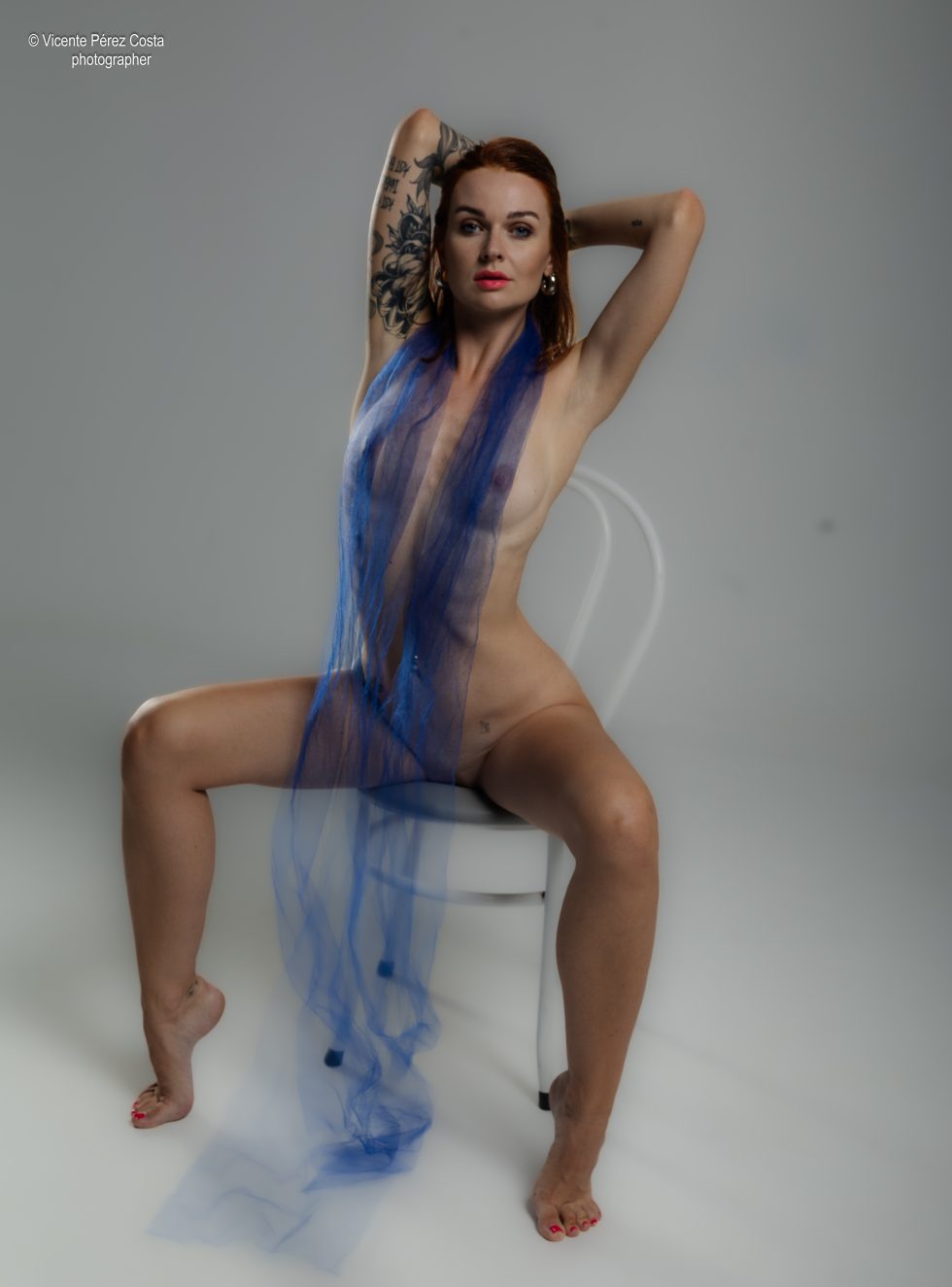 “Modelo posando en estudio con tela azul en una sesión de desnudo artístico, iluminada en clave suave y con estética minimalista.”