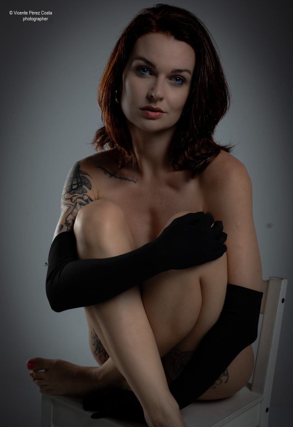 “Modelo posando en estudio con tela azul en una sesión de desnudo artístico, iluminada en clave suave y con estética minimalista.”