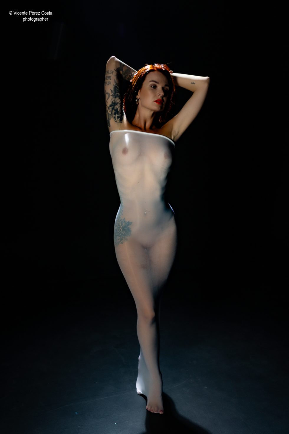 “Modelo posando en estudio con tela azul en una sesión de desnudo artístico, iluminada en clave suave y con estética minimalista.”