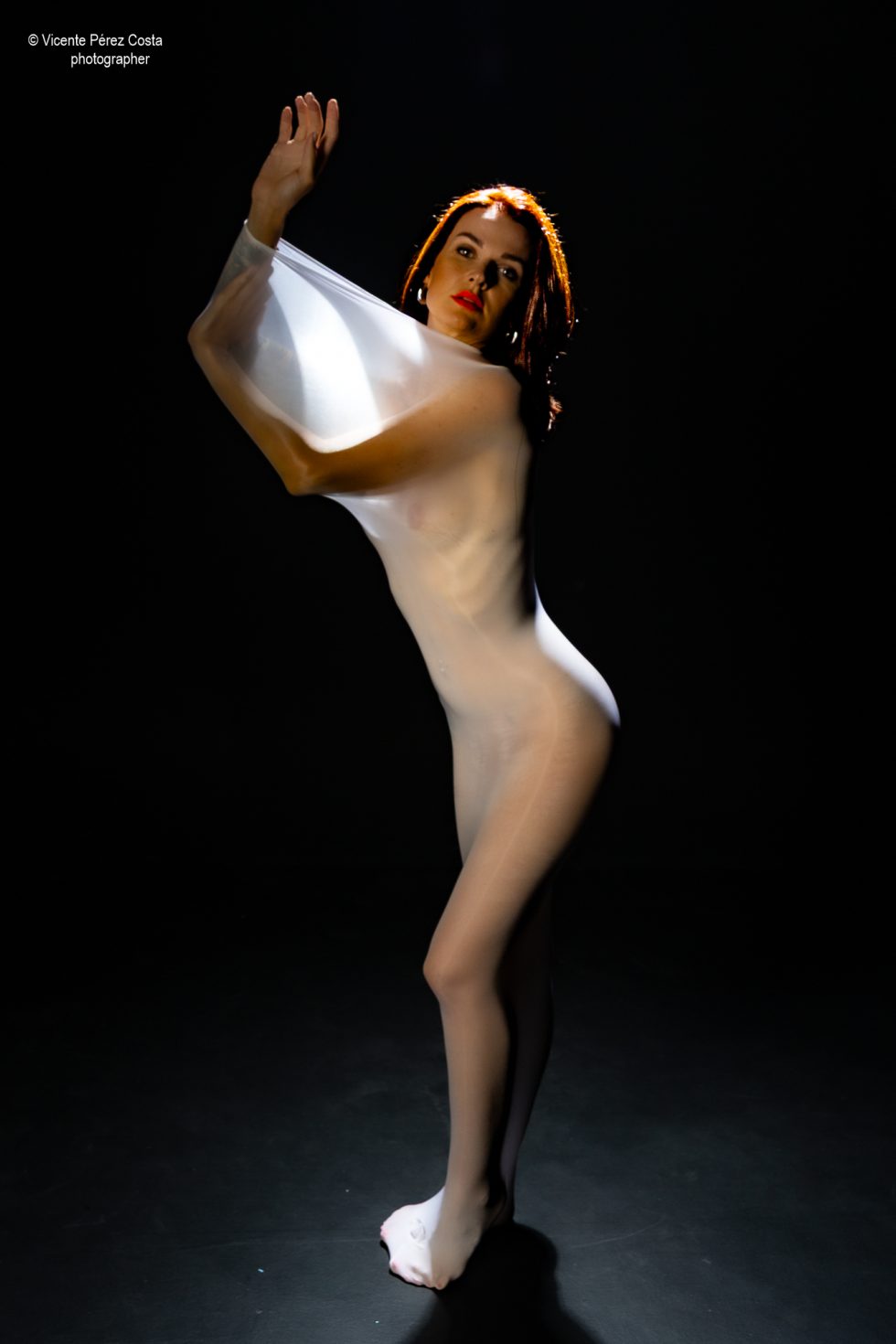 “Modelo posando en estudio con tela azul en una sesión de desnudo artístico, iluminada en clave suave y con estética minimalista.”