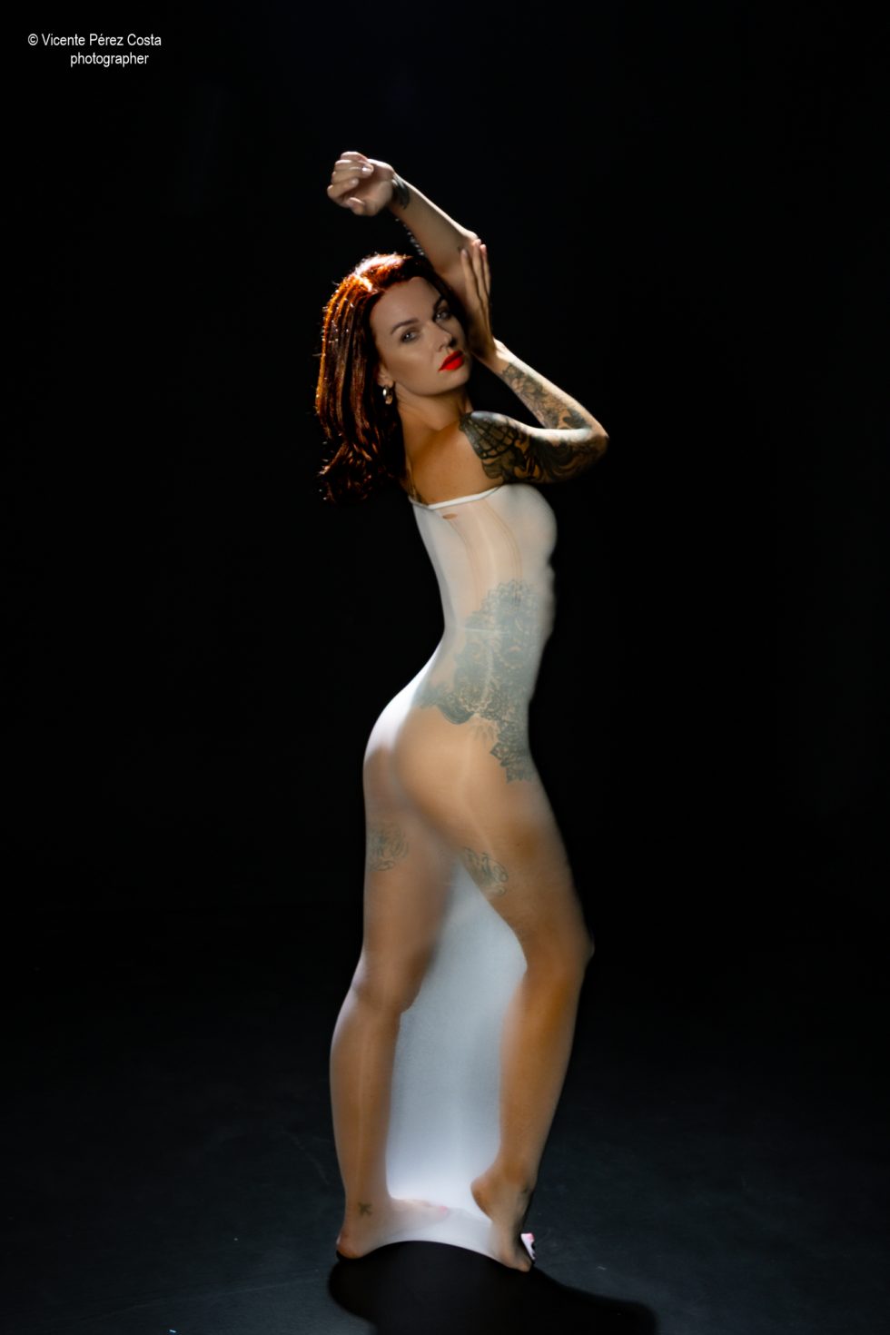 “Modelo posando en estudio con tela azul en una sesión de desnudo artístico, iluminada en clave suave y con estética minimalista.”