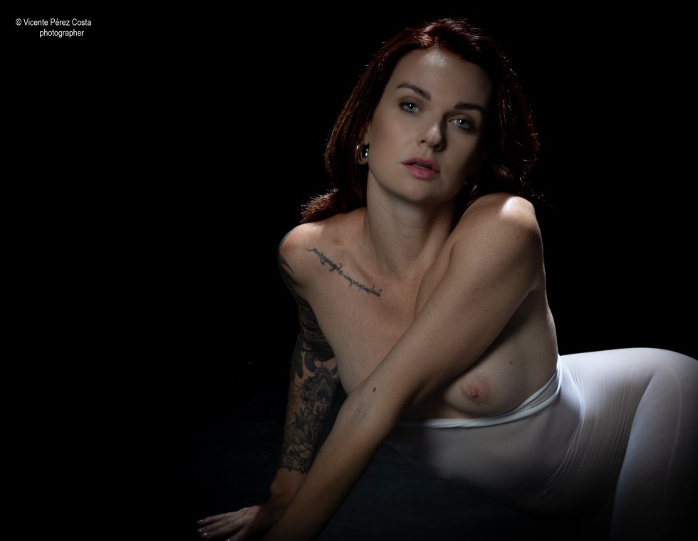 “Modelo posando en estudio con tela azul en una sesión de desnudo artístico, iluminada en clave suave y con estética minimalista.”