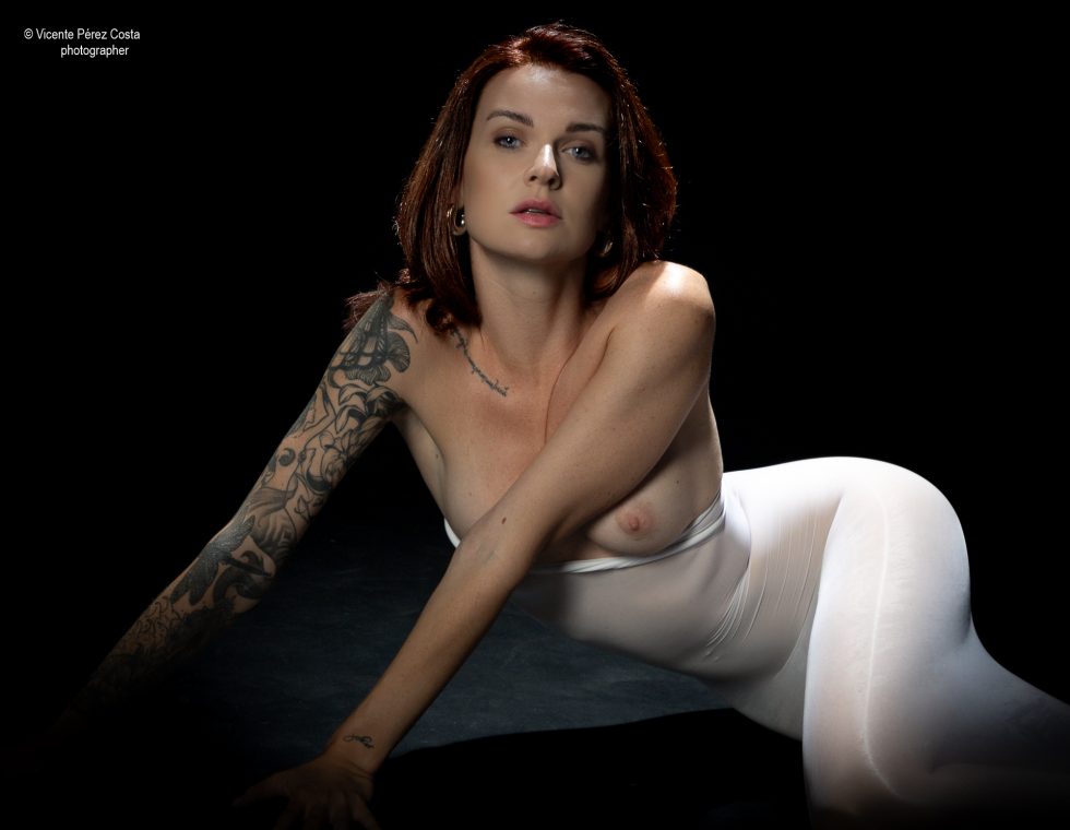 “Modelo posando en estudio con tela azul en una sesión de desnudo artístico, iluminada en clave suave y con estética minimalista.”