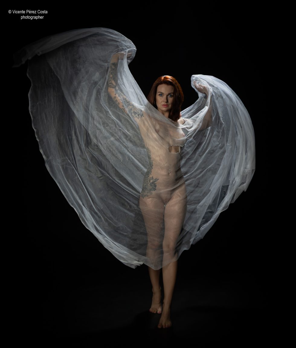 “Modelo posando en estudio con tela azul en una sesión de desnudo artístico, iluminada en clave suave y con estética minimalista.”