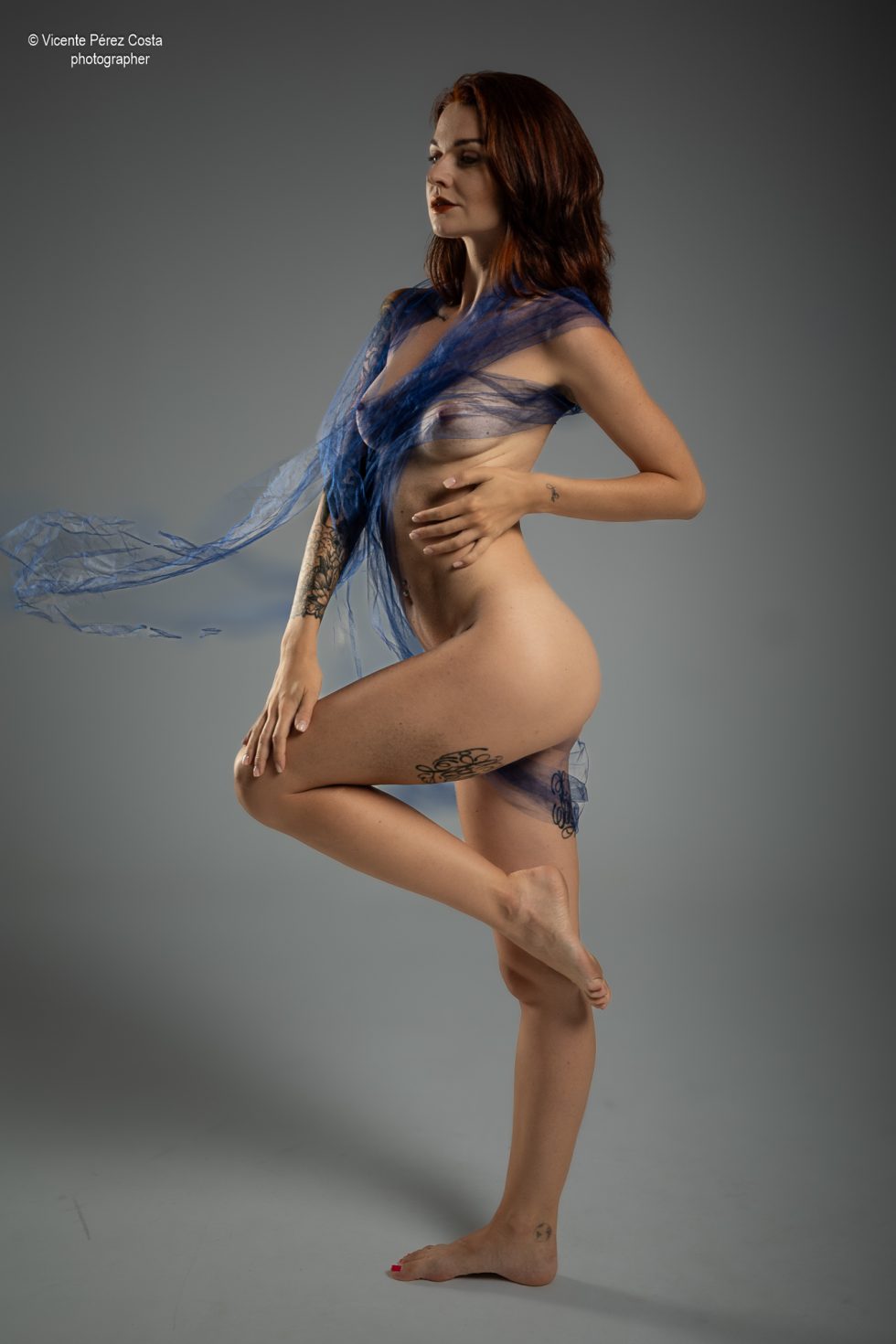 “Modelo posando en estudio con tela azul en una sesión de desnudo artístico, iluminada en clave suave y con estética minimalista.”