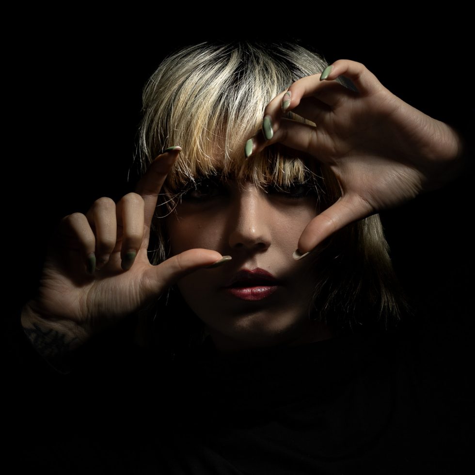 Rossana, modelo italiana, retrato artístico en clave baja con juego expresivo de manos y luz dramática sobre fondo negro.