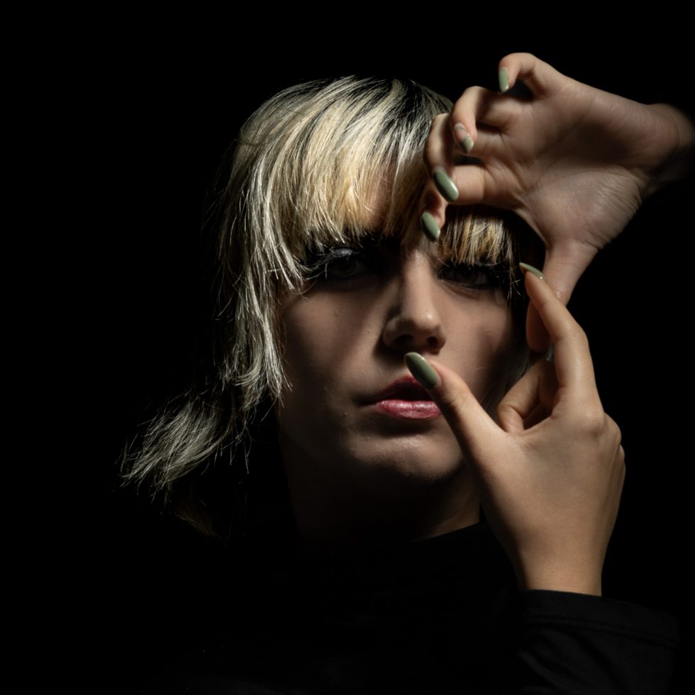 Rossana, modelo italiana, retrato artístico en clave baja con juego expresivo de manos y luz dramática sobre fondo negro.