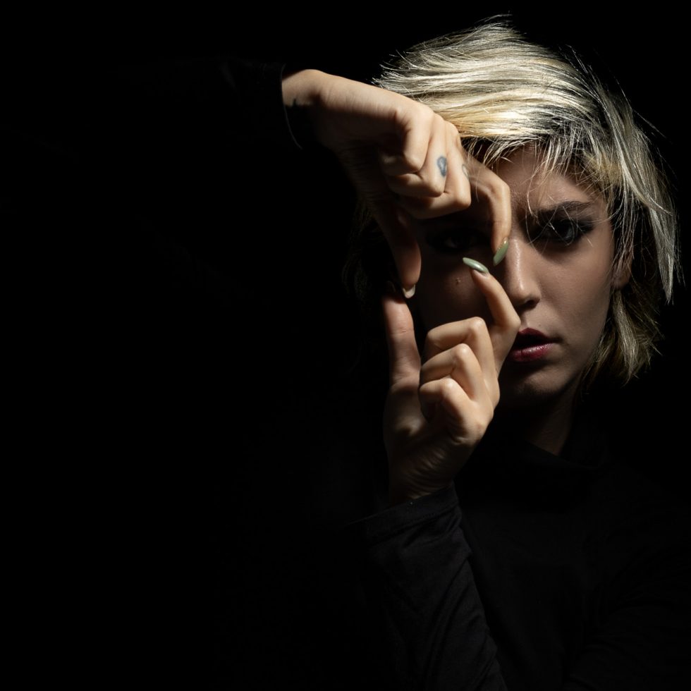 Rossana, modelo italiana, retrato artístico en clave baja con juego expresivo de manos y luz dramática sobre fondo negro.