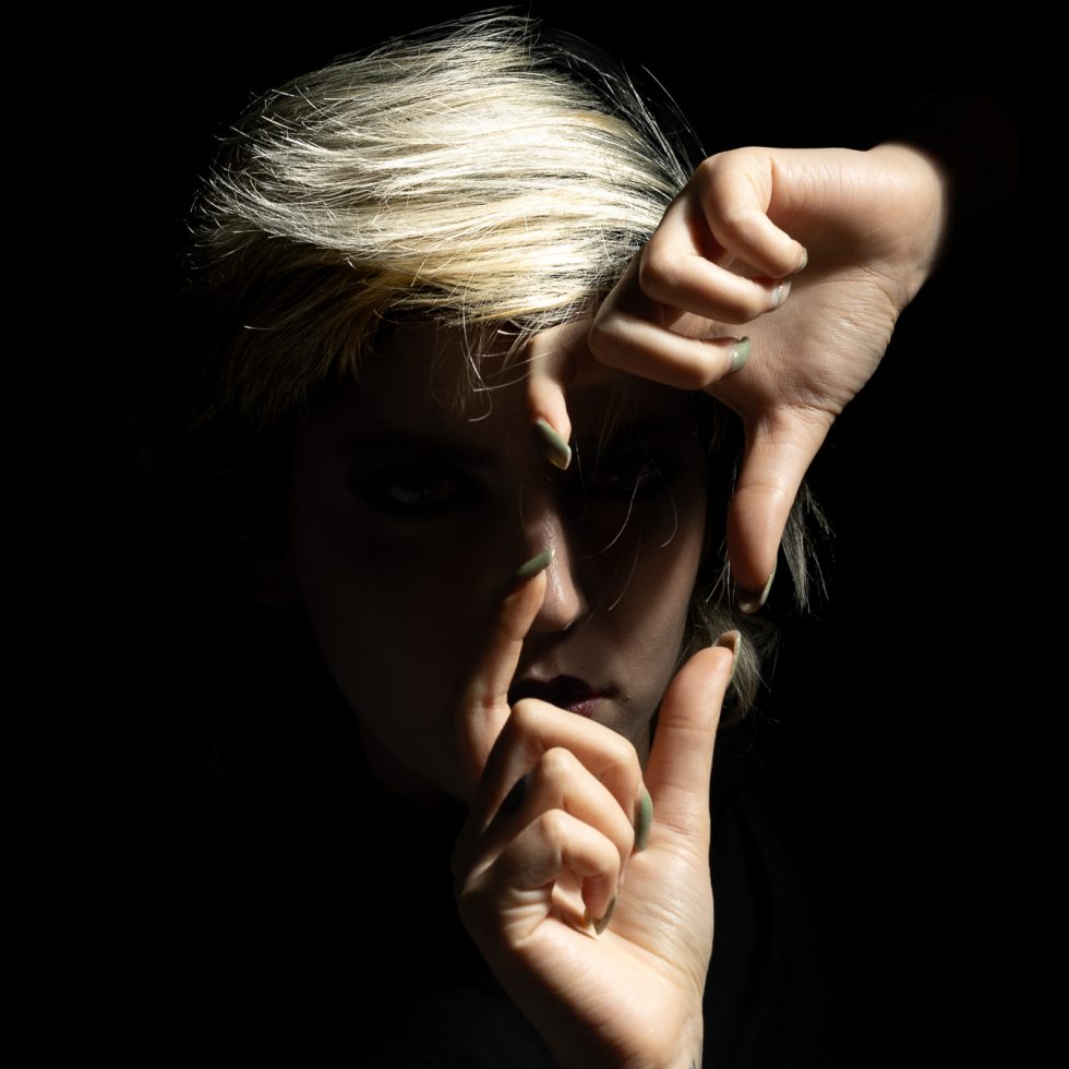 Rossana, modelo italiana, retrato artístico en clave baja con juego expresivo de manos y luz dramática sobre fondo negro.