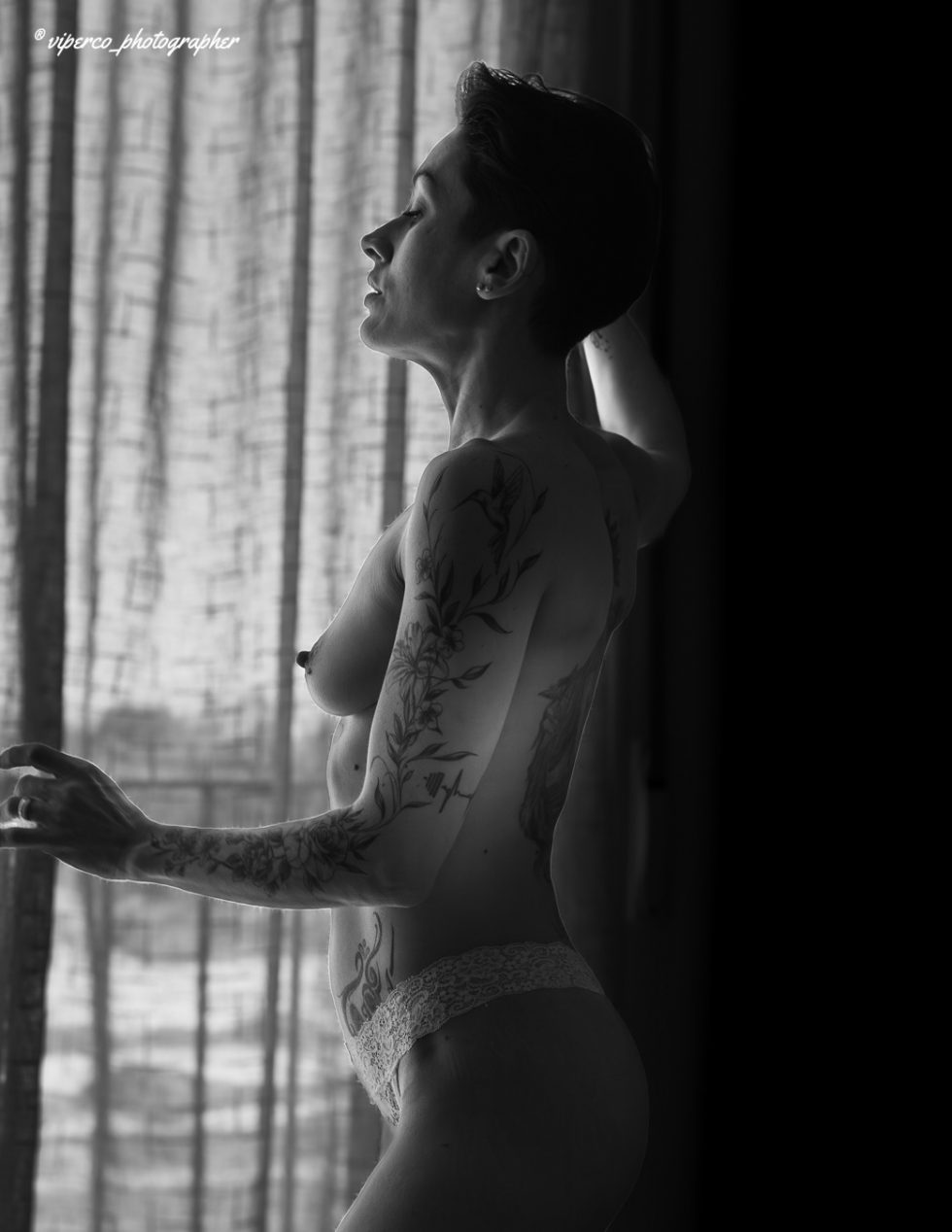 Mujer desnuda en blanco y negro junto a ventana, composición artística de sombras y luz