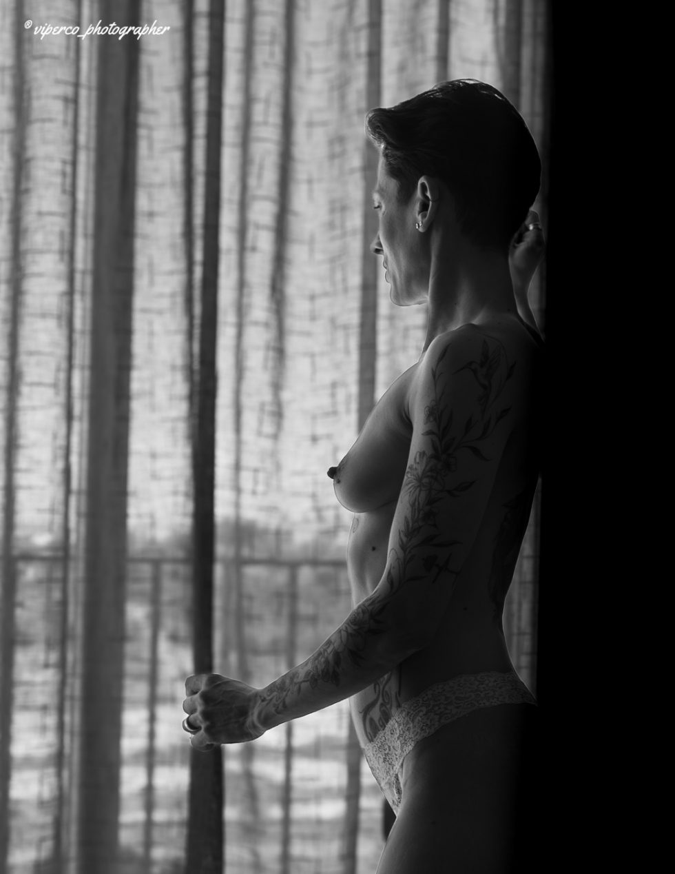 Mujer desnuda en blanco y negro junto a ventana, composición artística de sombras y luz