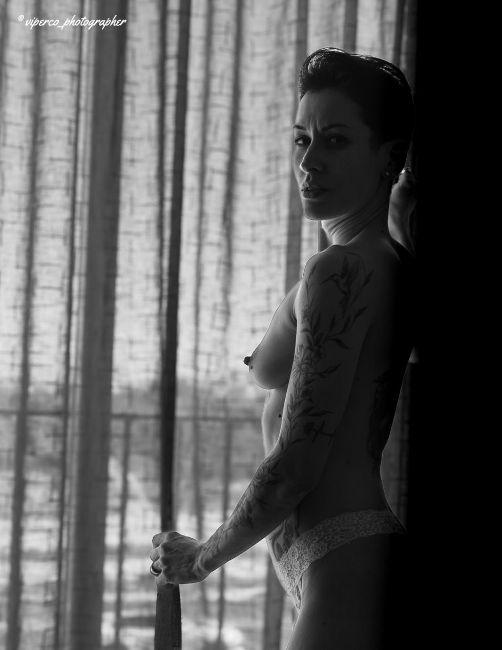 Mujer desnuda en blanco y negro junto a ventana, composición artística de sombras y luz